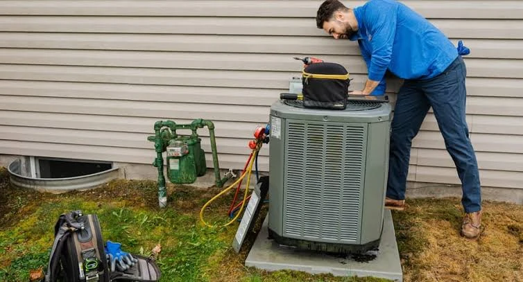 Technician servicing an outdoor air conditioner beside a home